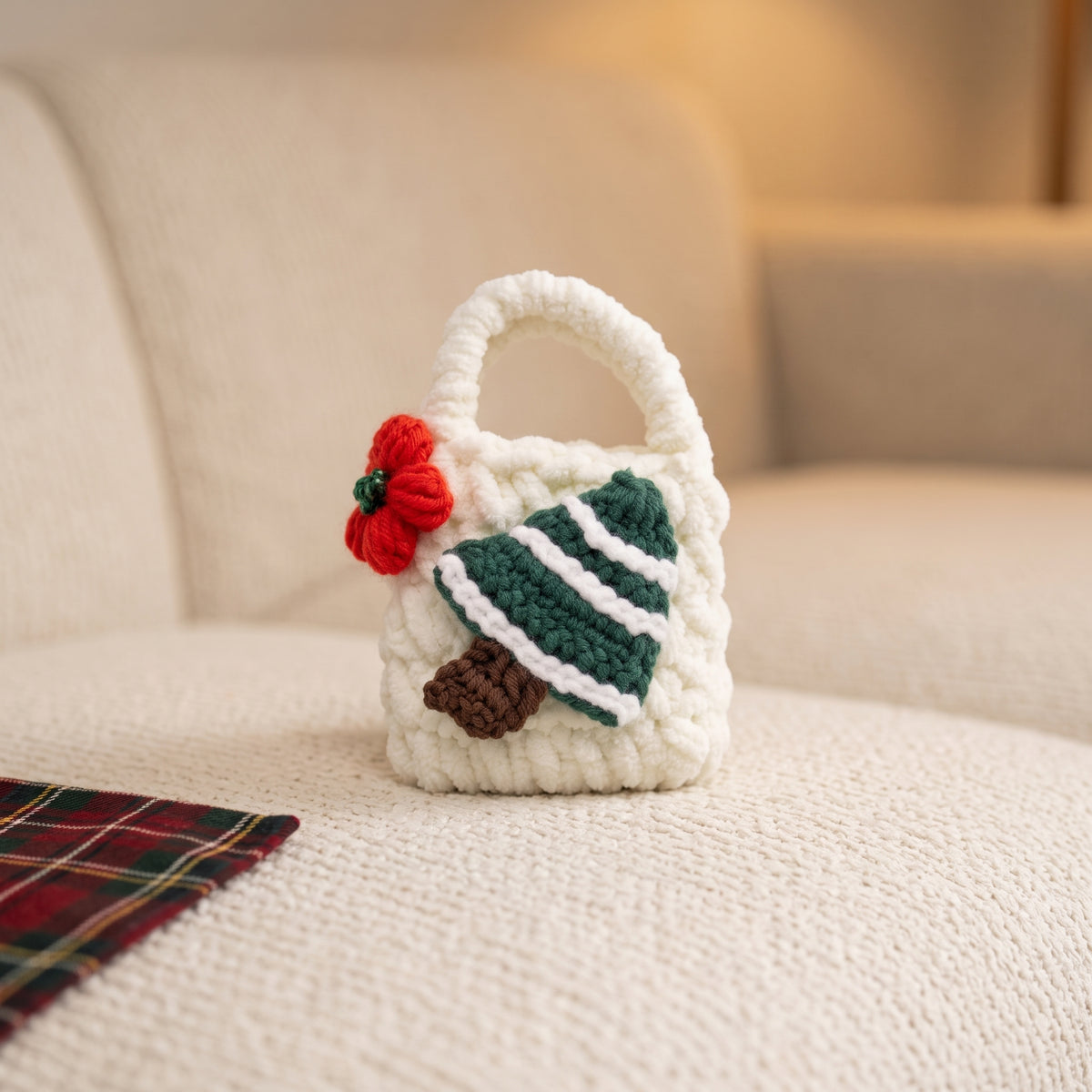 Close-up shot of a small white handmade crochet pouch, perfect for holding earbuds. It features a handcrafted green Christmas tree with white stripes and a charming red crocheted flower with green beads, complete with a loop handle, isolated against a light gray-white background.