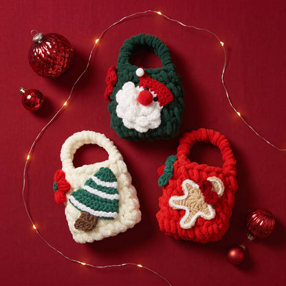 Three handmade crochet Christmas mini tote bags, Santa gnome, christmas tree and gingerbread man designs on deep red fabric with fairy lights and ornaments