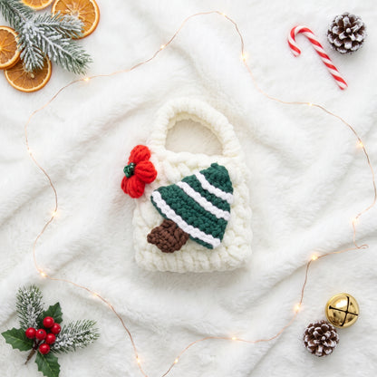 A charming, white knitted tech accessory pouch designed with a festive green Christmas tree and a small red knitted flower. The textured fabric and a functional small carrying handle are clearly visible, presenting a unique way to protect earbuds or small essentials.