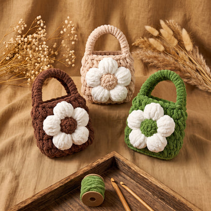 Top-down view of five small knitted earphone holders designed like mini tote bags with top handles and large white flower decorations, scattered near crafting thread spools.