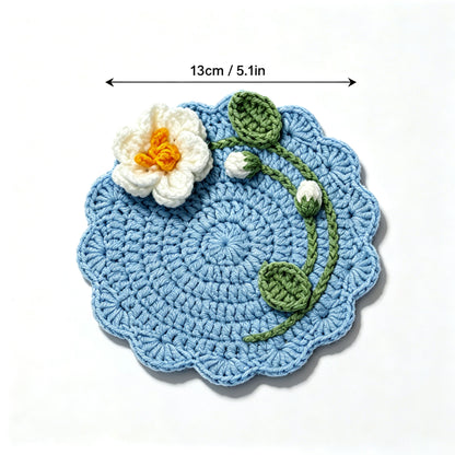 Handmade blue crochet flower coaster with white blossom and green leaves, size marked 13cm 5.1 inches, top view on white background, floral edge drink coaster