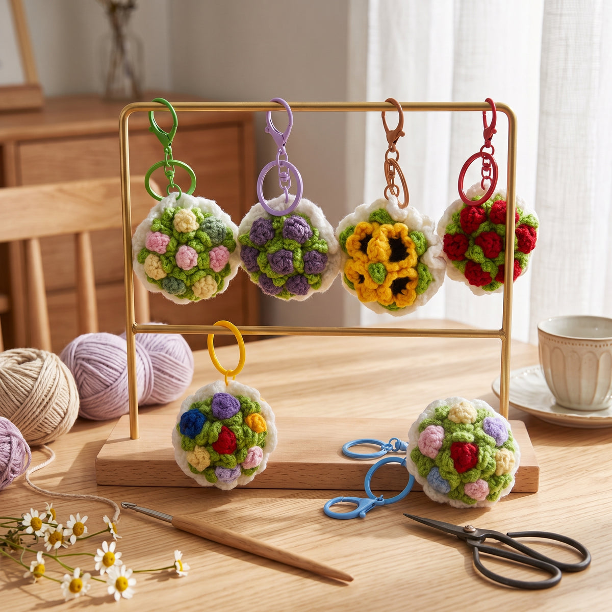 Handmade crochet bouquet keychains hanging on gold metal display rack, multicolor knitted flower key charms with yarn and crochet tools on wooden table