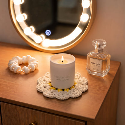 Beige handmade crochet flower coaster under a scented candle on wooden vanity table, elegant bedroom decor with perfume bottle and lighted round makeup mirror, cozy aesthetic scene