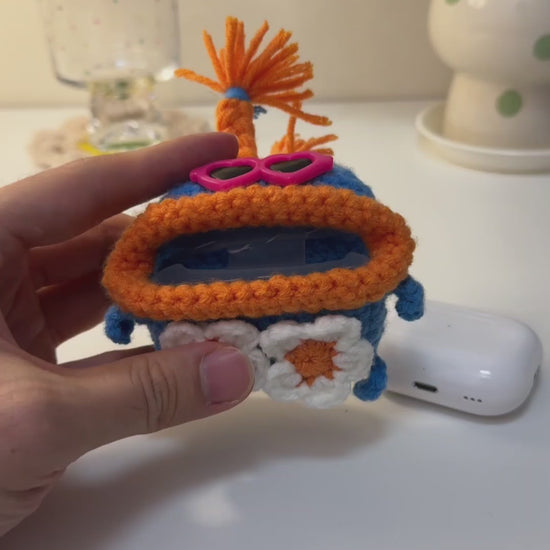 Handmade crochet monster AirPods case in blue and orange, with pink heart glasses and daisies